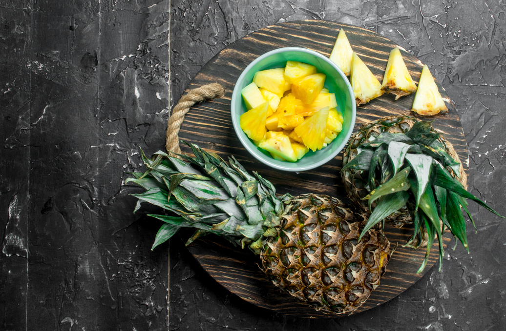 Slices of pineapple in a bowl and whole fresh pineapples on a tray.